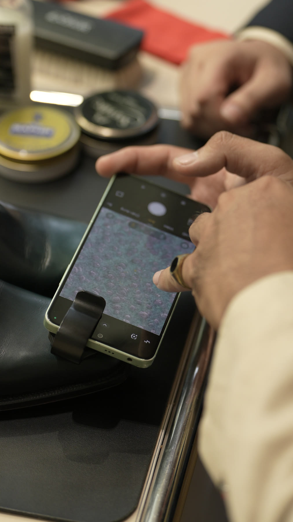 A clip-on microscope lens pressed against the leather, the magnified surface on the phone screen